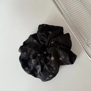 Detailaufnahme der plissierten Textur und des Punktmusters eines schwarzen Satin-Haargummis.