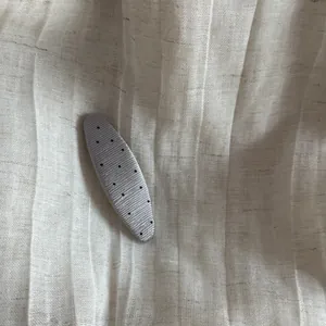 Macro view of silver textured hair clip with black polka dots on linen background
