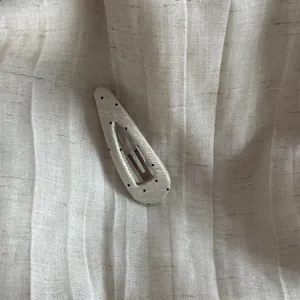 Detail view of a cream polka dot triangular BB hair clip on pleated fabric