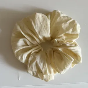 Detail eines übergroßen cremefarbenen Stoff-Haargummis mit dezenten bunten Sprenkeln.