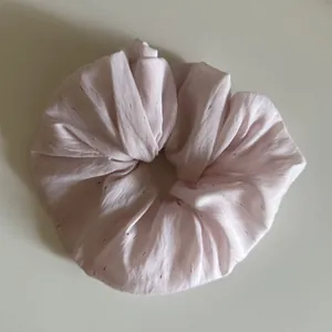 Detailansicht eines großen hellrosa Scrunchies mit bunt gesprenkelter Stofftextur.