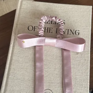 Detail van een oudroze satijnen haarelastiek met lange linten op een boek