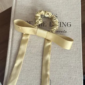 Detailopname van een champagne satijnen scrunchie met lange linten op een getextureerd boek.