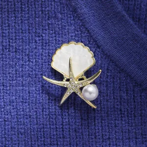Detailansicht einer eleganten Seestern- und Muschelperlenbrosche auf blauem Strick