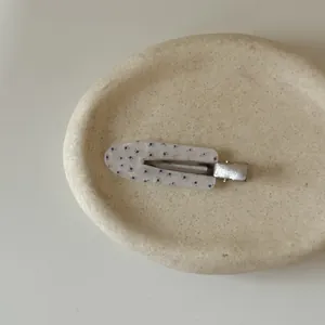 Detail view of a vintage floral pattern hair clip on a textured stone tray.