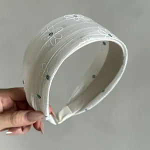 Detail view of a cream wide headband with white and blue daisy embroidery