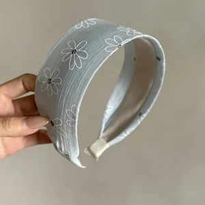 Close-up view of a wide light blue fabric headband with white embroidered daisy pattern.