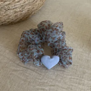 Close-up of a blue leopard print mesh scrunchie featuring a soft light blue heart charm.