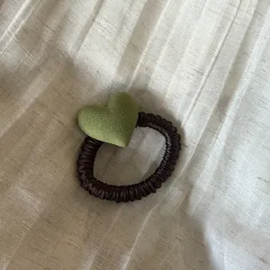Vista macro de un coletero de corazón de felpa verde sobre un elástico negro.