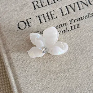 Close-up of a white flower acetate hair claw clip featuring a sparkling center rhinestone.