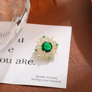 Vista detallada de un broche de flor vintage dorado con cristal verde esmeralda.