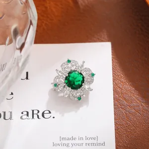 Detalle de un lujoso broche floral con un vibrante cristal verde esmeralda en el centro.