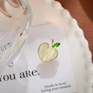 Close-up of small apple brooch with yellow heart stone and green rhinestone leaf.