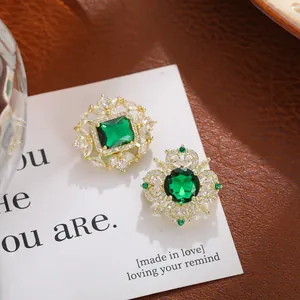 Primer plano de elegantes broches de cristal verde esmeralda en tarjeta blanca con oro.