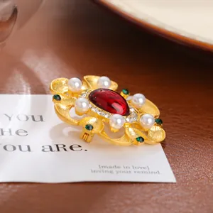 Gros plan d'une broche baroque dorée vintage avec pierre rouge et perles sur une carte.