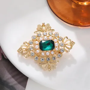 Detail of vintage emerald brooch with pearls and rhinestones in gold setting.