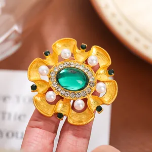 Gros plan détaillé d'une broche baroque en or avec pierres vertes et perles