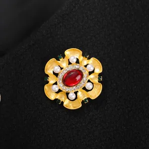 Gros plan d'une broche baroque dorée avec gemme rouge et perles sur tissu noir