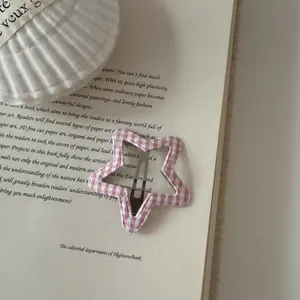 Macro detail of a pink gingham star-shaped hair clip resting on an open vintage book.