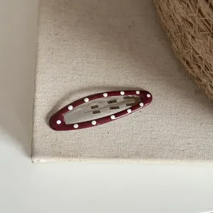 Vue détaillée d'une pince à cheveux ovale rouge à pois sur une surface en tissu texturé.