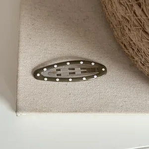 Détail d'une pince à cheveux ovale vert olive à pois blancs sur un fond en toile de lin.