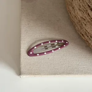 Gros plan d'une pince à cheveux ovale violette à pois blancs sur un fond en lin naturel