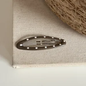 Gros plan d'une pince à cheveux ovale marron à pois blancs sur fond de tissu