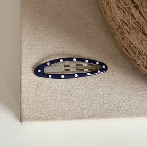 Gros plan d'une pince à cheveux ovale bleue à pois blancs sur fond en lin beige
