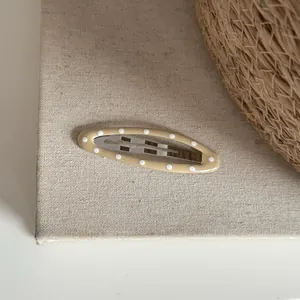 Vue détaillée d'une barrette ovale beige à pois blancs sur fond en tissu texturé