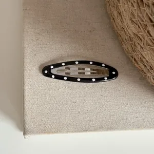 Vue détaillée d'une barrette ovale noire ornée d'un motif classique à pois blancs.