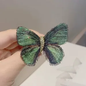 Gros plan d'une broche papillon brodée en dégradé vert avec corps en alliage doré.