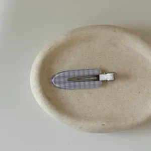 Close-up detail of a purple and white checkered hair clip on a minimalist stone display