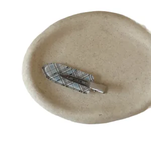 Blue plaid pattern hair clip with metal base displayed on a textured ceramic tray