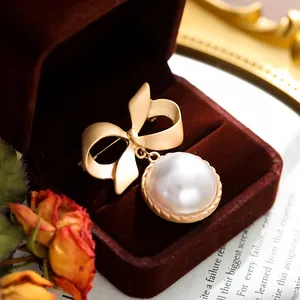 Dettaglio macro di un'elegante spilla vintage a fiocco dorato con ciondolo di perla