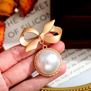 Dettaglio di una spilla a fiocco d'oro vintage con un grande ciondolo di perla bianca