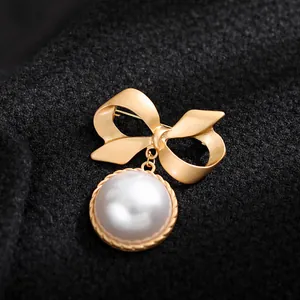 Primo piano dettagliato di una spilla a fiocco dorata vintage con pendente in perla bianca
