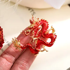 Vista detallada de un broche de dragón chino dorado con esmalte rojo sobre un fondo cálido