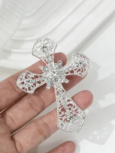 Detailaufnahme einer silbernen Strass-Kreuzbrosche mit filigranem Design in der Hand
