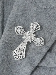 Elegante Kreuzbrosche mit funkelnden klaren Strasssteinen auf grauem Wollstoff Textur