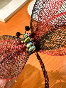 Detailopname van een elegante libellebroche met rood-zwarte gaasvleugels en kristallen.