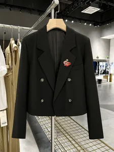 Detalle de un broche de flamenco rosa y rojo prendido en la solapa de un blazer negro.