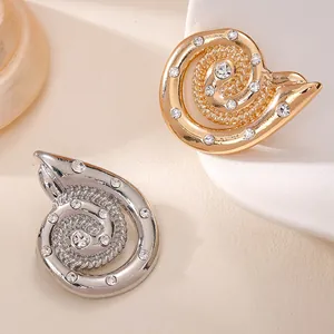 Detail der spiralförmigen Muschelbroschen in Gold und Silber mit Strasssteinen.