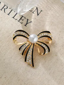 Nahaufnahme einer eleganten goldenen Schleifenbrosche mit schwarzer Emaille und Perle
