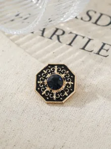 Macro detail of a vintage gold lapel pin featuring black enamel and a blue crystal