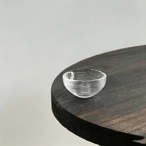 Minimalist Japanese transparent glass tea cup with ripple texture on a wooden table.