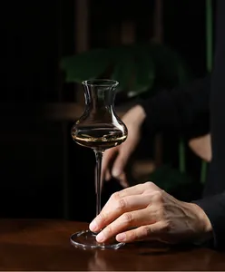 Close-up of a tulip-shaped crystal liqueur glass held by hand in a dark setting.
