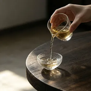 Japanese clear glass tea cup set on a rustic wooden table with tea pouring 45-degree angle.