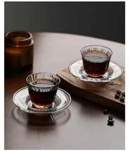 Detailed view of two embossed glass tea cups and saucers on a wooden tray
