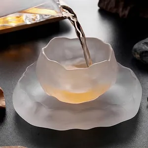 Macro shot of tea being poured into a frosted glass teacup with a matching saucer.