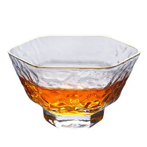 Minimalist hand-blown hexagonal glass teacup with hammered texture and gold rim.